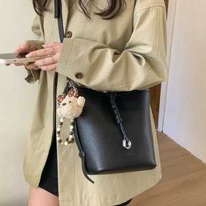 Detail of black lychee leather bucket bag with woven drawstring and cute bear charm