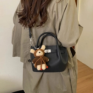 Detail of black lychee grain leather crossbody bag with silver lock and bear charm