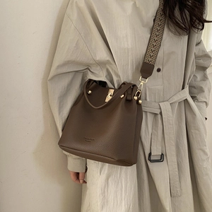 Detail of brown leather bucket bag with litchi grain and geometric woven shoulder strap