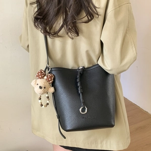 Detail of black lychee grain bucket bag with woven decor and plush bear charm