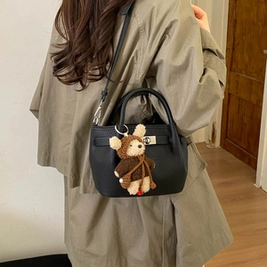 Detail of black pebbled leather bucket bag with metal lock and cute teddy bear charm
