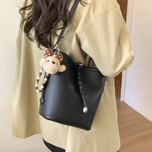 Detail of black pebbled leather bucket bag with plush bear charm and beaded handle
