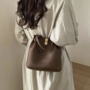 Detailed view of textured dark brown leather bucket bag with gold hardware worn on shoulder