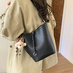 Detail of black lychee grain bucket bag with a cute bear pendant and silver hardware