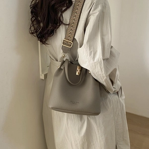 Detail of greige lychee leather bucket bag with patterned wide strap and gold hardware