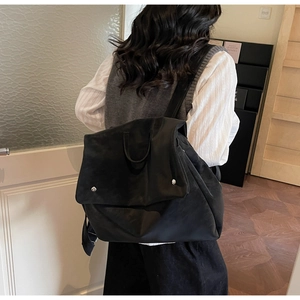 Detail of a black nylon backpack with flap closure and silver buttons on model in room