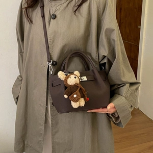 Detail of dark brown leather bucket bag with turn-lock and cute crochet bear charm