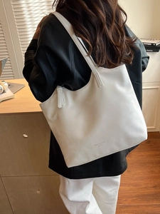 Minimalist white leather tote bag with embossed text shown on a female model shoulder