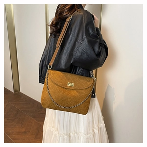 Nahaufnahme der gesteppten braunen Wildledertasche mit Goldkette und Verschluss am Modell