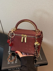 Burgundy woven box bag with gold metal handle and cherry charm pendant details