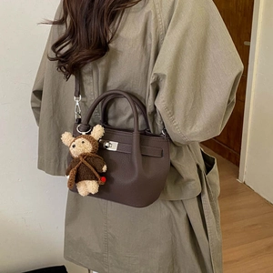 Detailed side view of dark brown pebbled leather bucket bag with a cute teddy bear charm