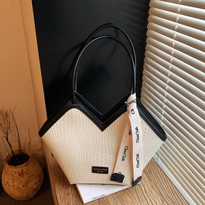 Detailed view of woven cream tote bag with black V-shaped trim and decorative ribbon