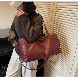 Détail macro de la texture du cuir PU bordeaux et du logo gaufré sur le sac de voyage