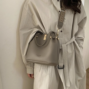 Detail of grey bucket bag featuring lychee grain leather and bohemian woven shoulder strap