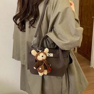 Detail of dark brown leather bucket bag with silver clasp and cute plush bear charm
