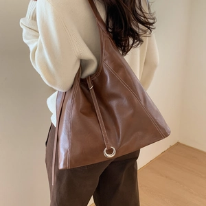 Detail of a brown leather tote bag with white contrast stitching and a metal ring pull