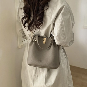 Detail of taupe litchi grain leather bucket bag with golden twist lock and brand logo