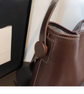 Detail of brown leather bucket bag with white contrast stitching and round button