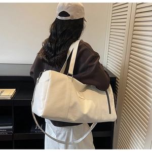 Détail du sac de sport crème avec texture litchi et boucles métalliques sur la bandoulière