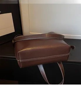 Detail of a brown bucket bag showing white contrast stitching and the sleek side profile
