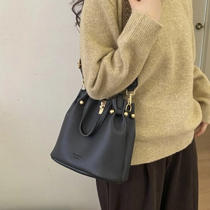 Detail of black lychee grain leather bucket bag with golden hardware and wide fabric strap