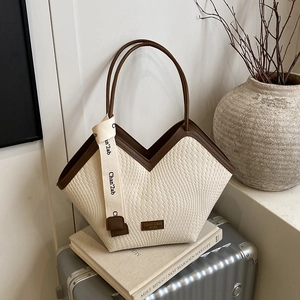 Detail of cream woven tote bag with brown leather handles and decorative brand strap