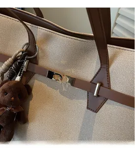 Detailed close-up of gold metal clasp on beige canvas tote bag with brown leather accents