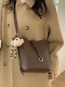 Brown leather bucket bag with braided handle and plush bear charm for casual wear