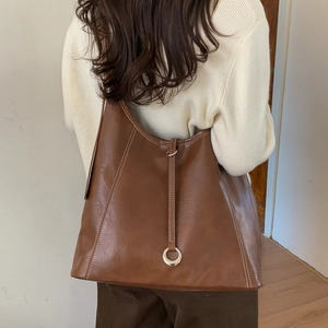 Detail of a large brown faux leather tote bag with white stitching and metal ring charm