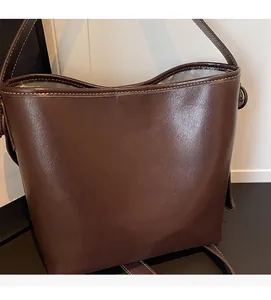 Detail view of brown leather bucket bag featuring white contrast stitching and gold pendant