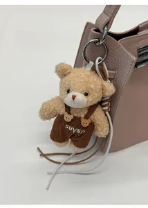 Close-up of a beige teddy bear charm in brown corduroy overalls on a pink bucket bag