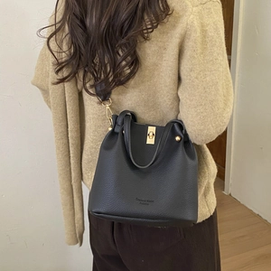 Detail of black lychee grain leather bucket bag with gold twist lock and shoulder strap