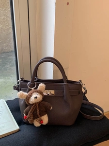 Deep brown pebble leather bucket bag with metal clasp and plush bear charm on black base
