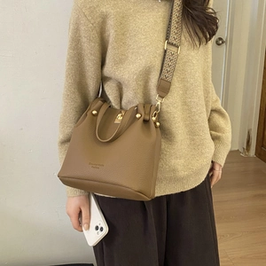 Detail of brown lychee grain leather bucket bag with vintage ethnic woven strap and gold hardware