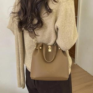 Detail of tan pebble leather bucket bag with gold hardware worn on model shoulder