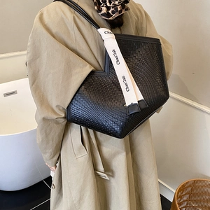 Close-up of black woven tote bag with designer ribbon on a stylish beige trench coat