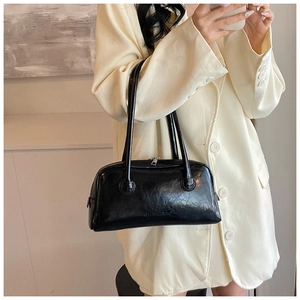 Detail of glossy black Boston bag with slim handles worn over a beige oversized blazer