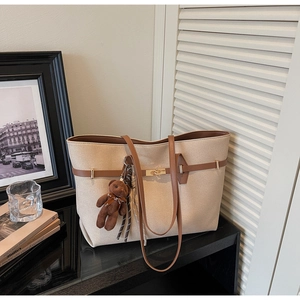 Detail view of beige tote bag with brown straps, metal turn-lock and plush bear charm