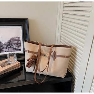 Detail of beige tote bag with brown handles and a cute teddy bear charm in a lifestyle set
