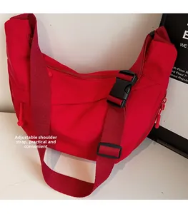 Détail de la boucle de bandoulière noire réglable sur un sac besace en nylon rouge