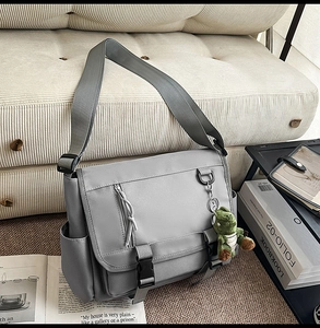 Detailed view of large grey nylon messenger bag with buckle straps and dinosaur charm