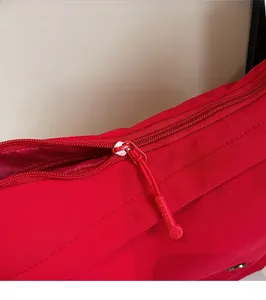 Détail macro du sac en nylon rouge montrant le zip en métal lisse et le logo de la marque