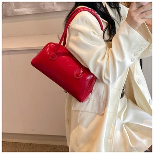Close-up of vibrant red patent leather shoulder bag held by a model in a white blazer