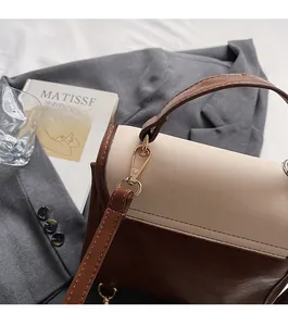 Detalle de bolso de cuero bicolor vintage con herrajes dorados sobre fondo de traje gris