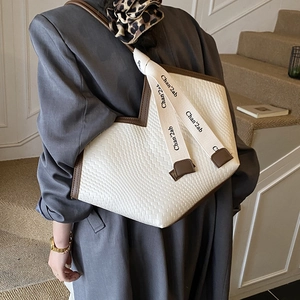 Detail of white woven tote bag with brown leather trim and lettered strap on shoulder