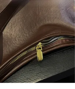 Dettaglio borsa in pelle marrone con cerniera dorata e fodera interna a righe