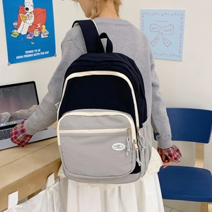 Detail view of the black and grey color-blocked backpack with white piping and logo