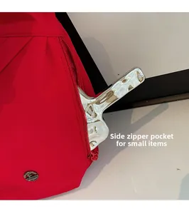Détail du sac bandoulière en nylon rouge avec poche latérale zippée et logo en métal