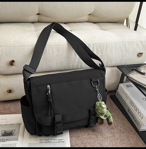 Detail of waterproof black messenger bag with adjustable strap and dinosaur pendant