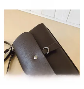 Close-up of deep coffee textured leather bag with metallic ring buckle and silver rivets